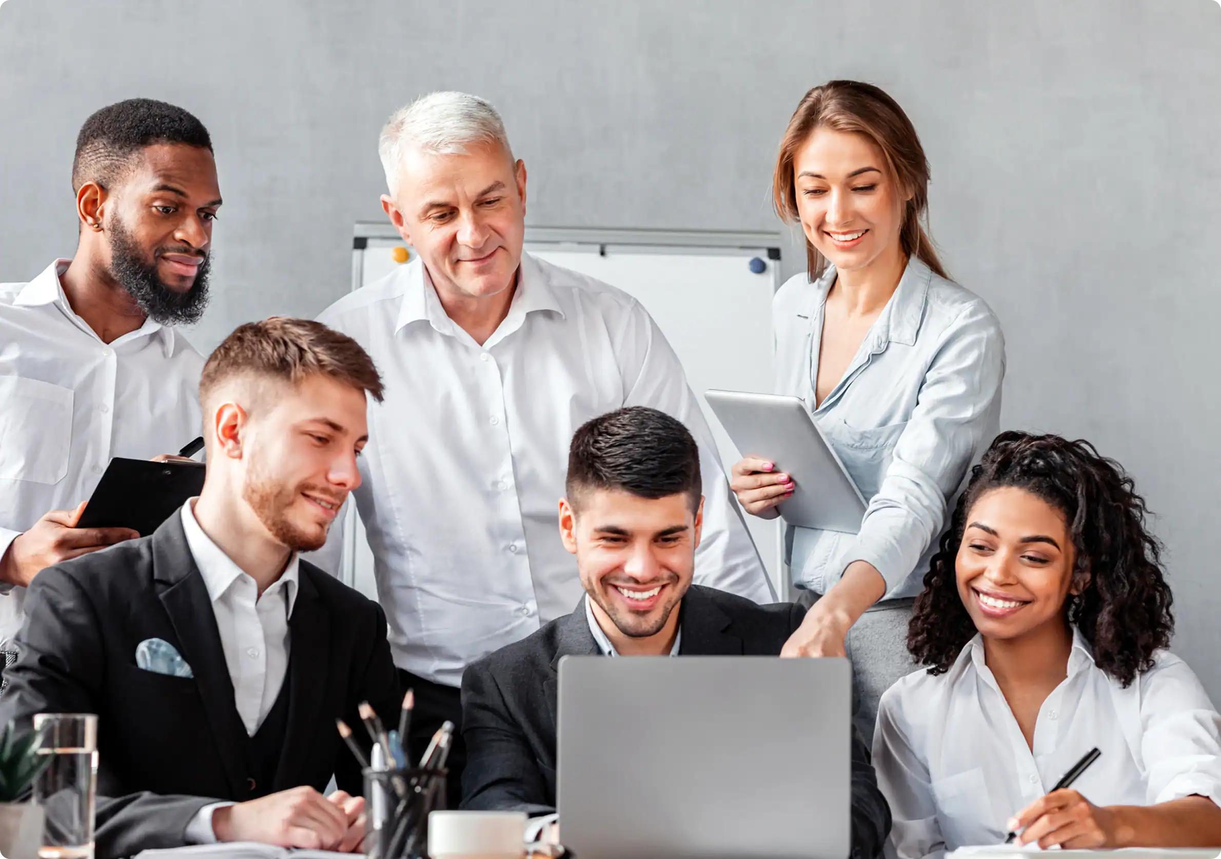 A diverse and smiling team of professionals collaborating around a laptop, representing the successful business transformation delivered through Nearshore IT Outsourcing Services.